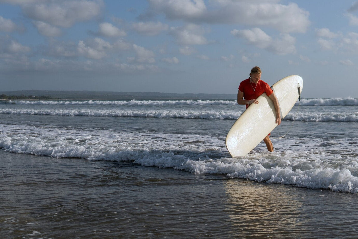 Surfer carrying a white longboard out of the shallows on an overcast beach