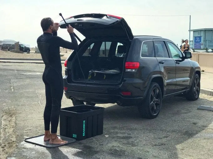 Surfer in a wetsuit standing on a BeachBox mat at the open boot of an SUV