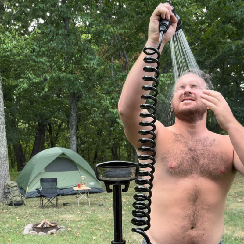 Man using a Beachbox portable shower outdoors with a tent and trees in the background.