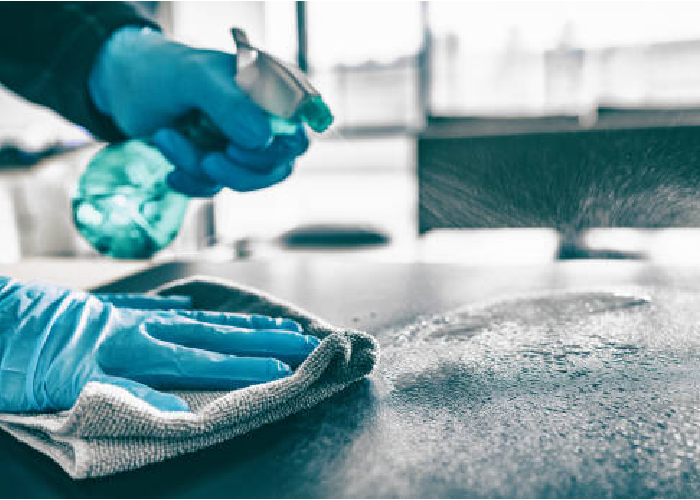 Gloved hands spraying disinfectant and wiping down a dark countertop with a cloth