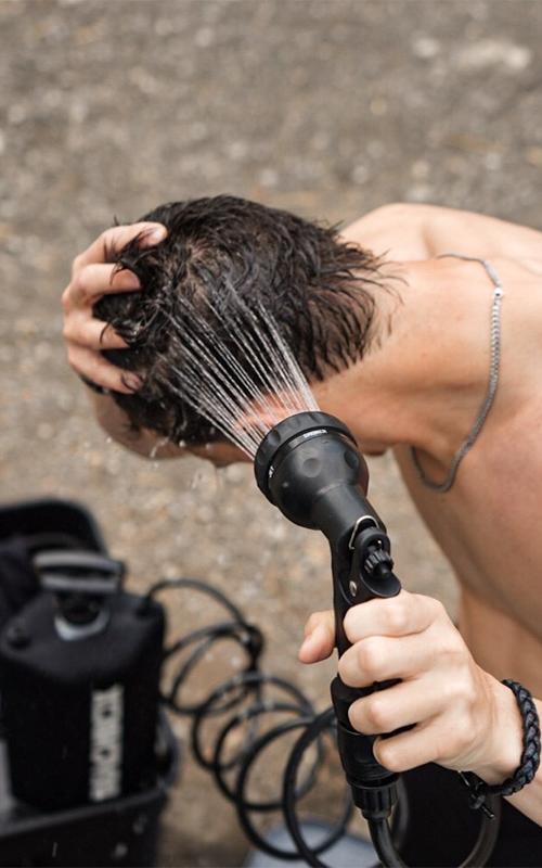 Man rinsing his hair with the spray nozzle of a BeachBox portable outdoor shower