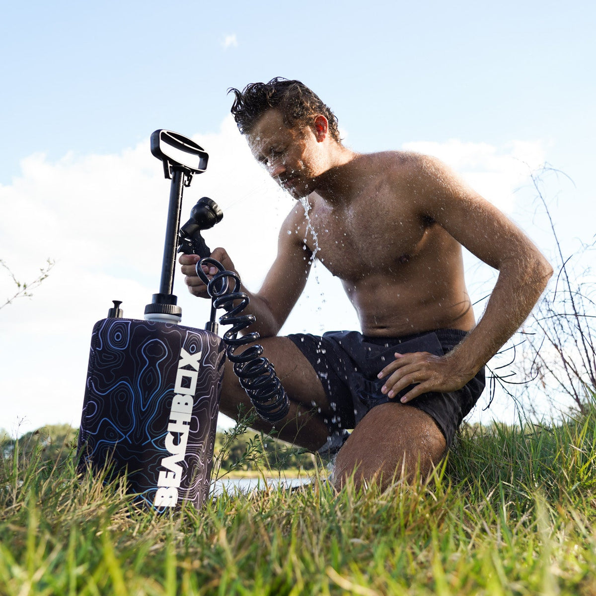 Man sitting on grass showering with BeachBox Shower Tank - Elevation